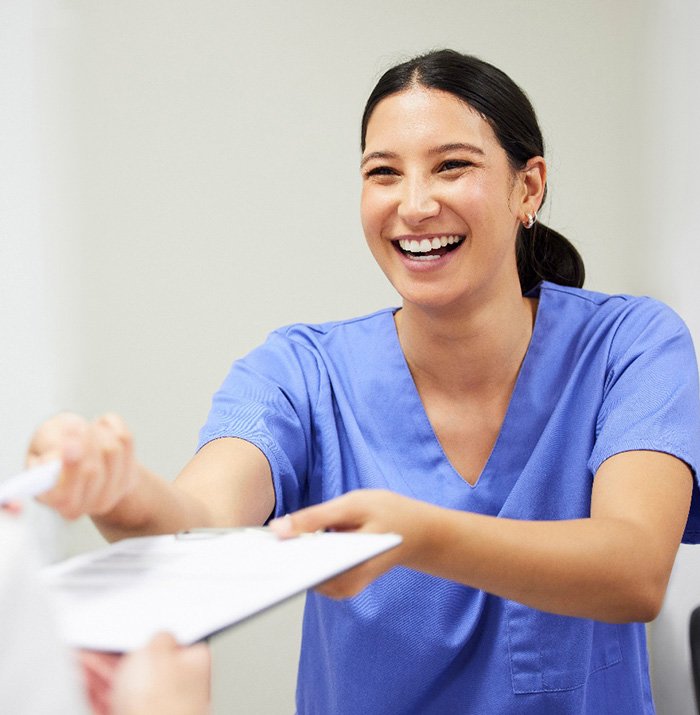 Smiling dental assistant handing patient forms