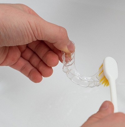 Patient cleaning clear aligner in sink