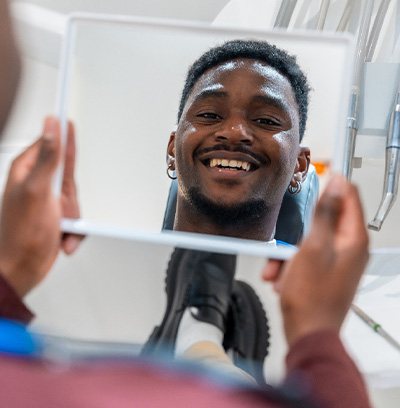 Man smiling at reflection in handheld mirror