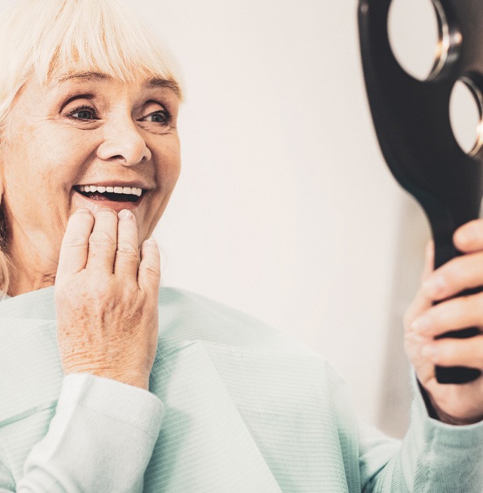 An older woman admiring her new dentures with a hand mirror