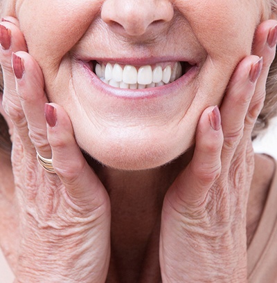 Nose-to-neck view of older woman smiling with both hands pressed to her cheeks