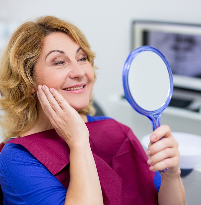 woman looking at her new smile in a mirror