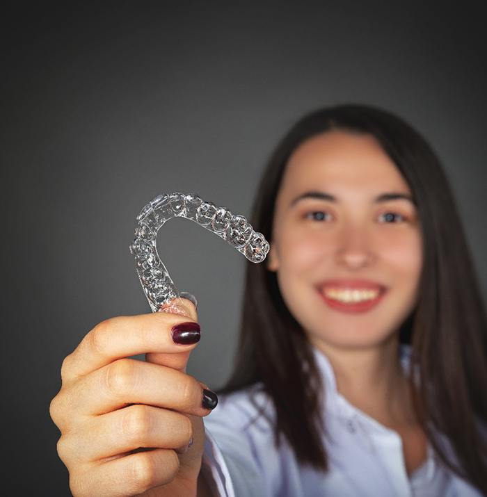 Woman holding a clear aligner for Invisalign.