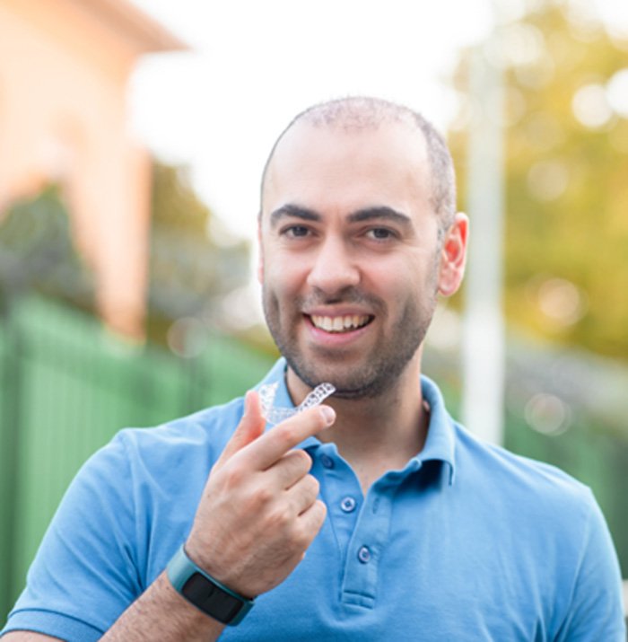 Man in blue shirt smiling outside with Invisalign aligner