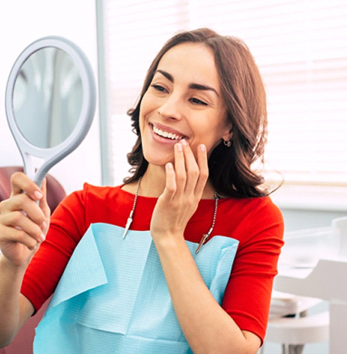 Woman with straight teeth smiling into hand mirror