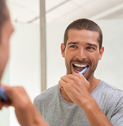 Man smiling while brushing his teeth in bathroom