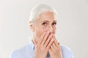 older woman covering mouth in shame