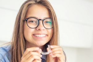 Smiling young woman in glasses holding Invisalign clear aligners