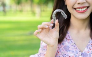 Smiling woman holding aligners isn't wondering "Does Invisalign hurt?"