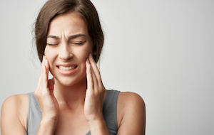 woman with toothache gritting teeth, hands to jaw, white background