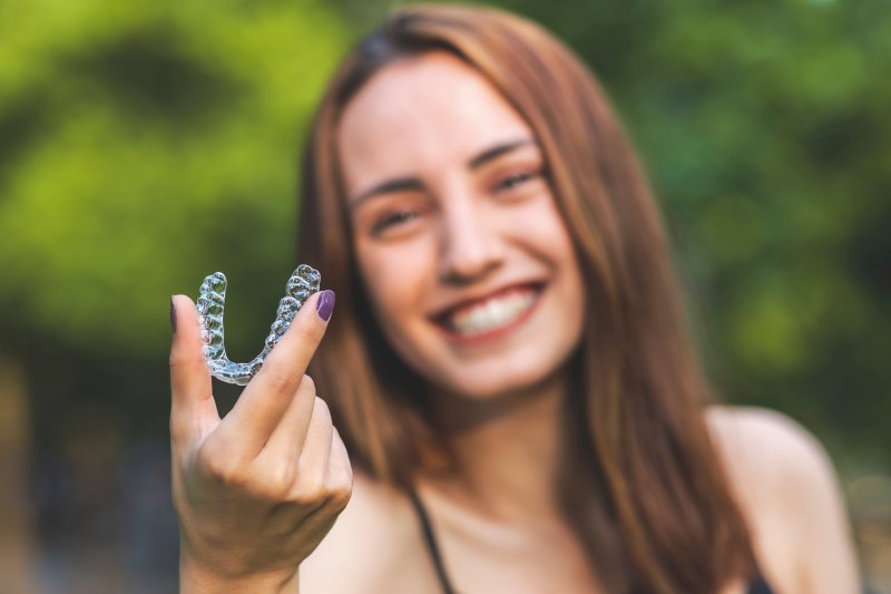 Smiling young woman holding Invisalign aligner