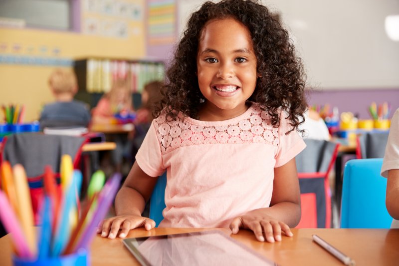 Child smiling in a classroom with tablet on table