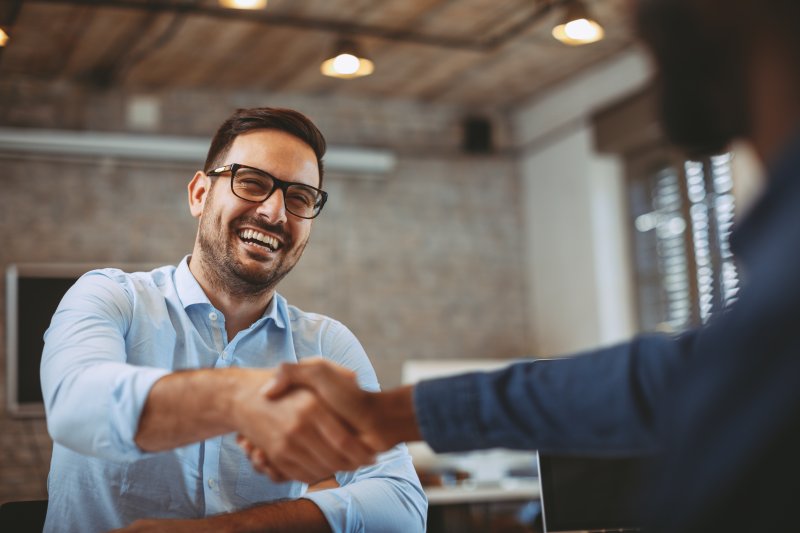 A man smiling as he shakes hands with his boss after his cosmetic dentistry