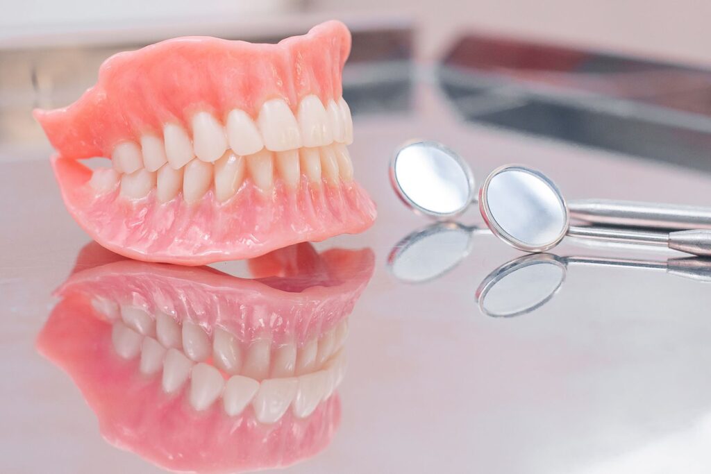 Complete set of dentures next to dental mirror on reflective metal tray