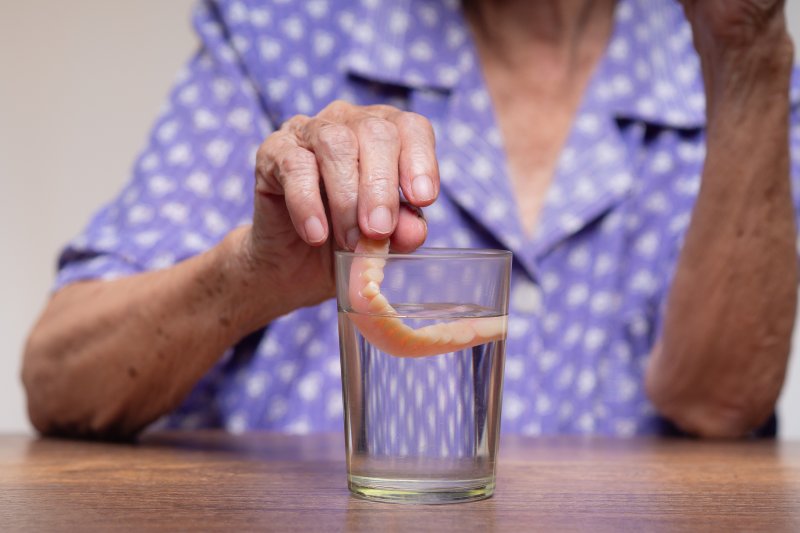 An elderly woman putting her denture in a glass of water